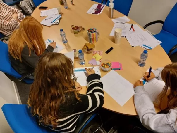 Meiden zitten aan een tafel en vullen een boekje in over hun mentale gezondheid.