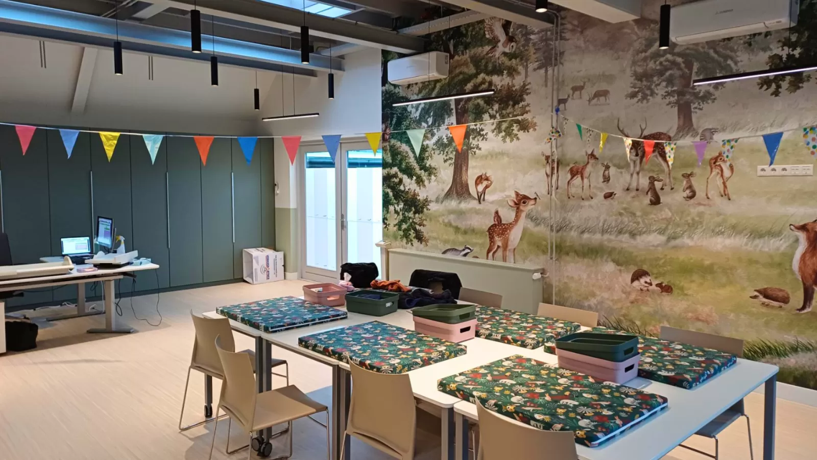 Interieur van het consultatiebureau in Soest met daarop gekleurde vlaggen en een muur met behang van bosdieren.